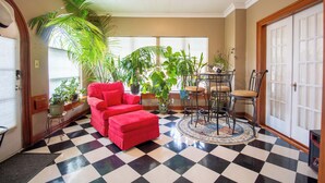Ein Zimmer mit Schachbrettmuster-Boden, einem roten Sofa, einem Esstisch mit Stühlen und einigen Kübelpflanzen.