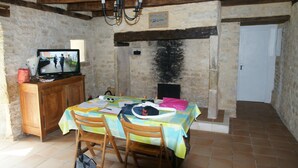 A rustic dining area with a wooden table, chairs, and a television on a wooden cabinet. - Former sheepfold in the middle of an orchard and a 2 ha meadow (Ussel)