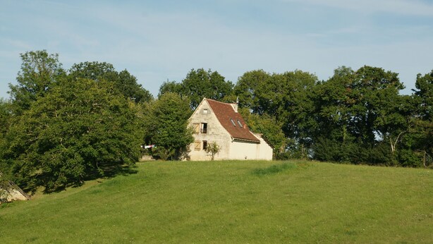 A single-story house with a sloped roof, surrounded by a grassy field and dense trees. - Former sheepfold in the middle of an orchard and a 2 ha meadow (Ussel)