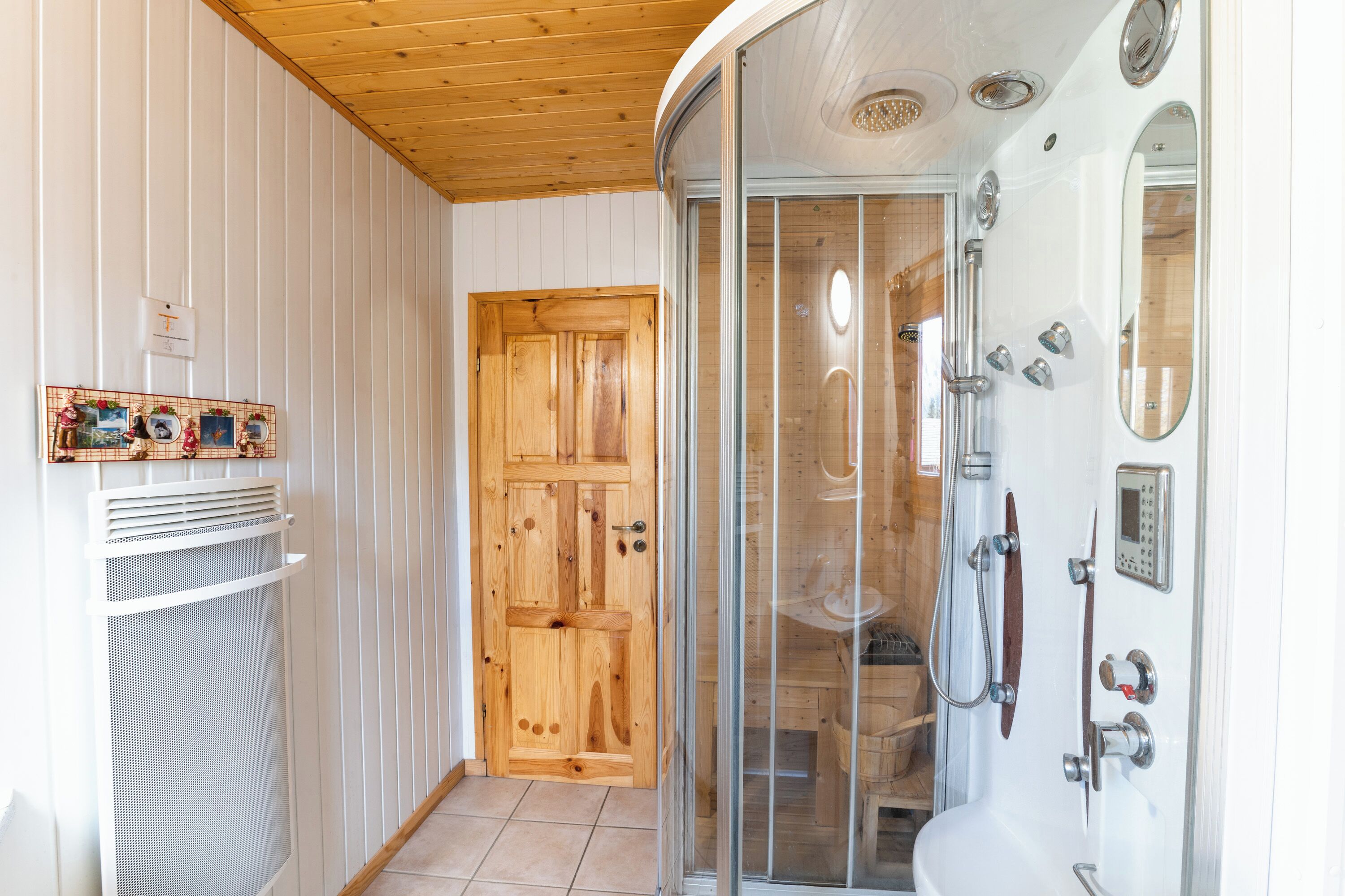 Une salle de bain avec une douche à parois de verre, une porte en bois et un radiateur blanc.