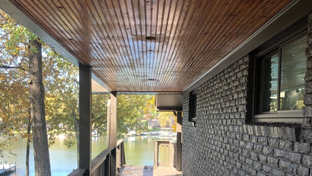 A covered wooden deck with a brick wall on one side and a view of a lake.