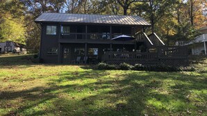 A two-story cabin with a balcony, surrounded by trees and a grassy yard.
