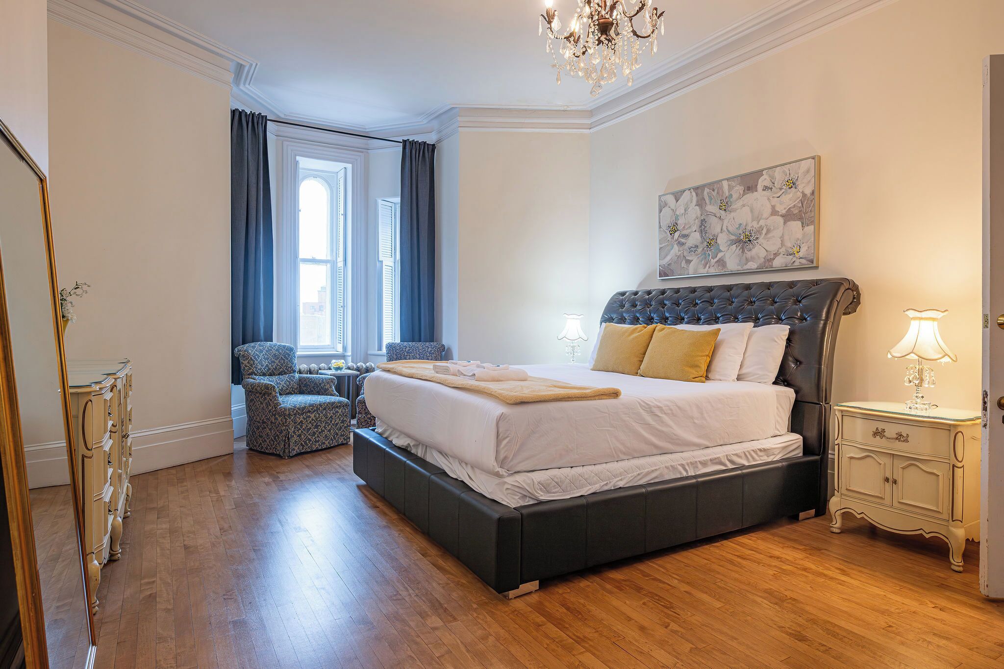 A bedroom with a large bed, a dresser, a chair, and a window with curtains.