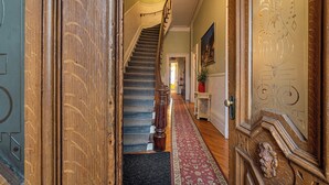 Eine imposante Treppe führt zu einer zweiten Etage, gesäumt von verzierten Holztüren und einem roten, gemusterten Teppich.