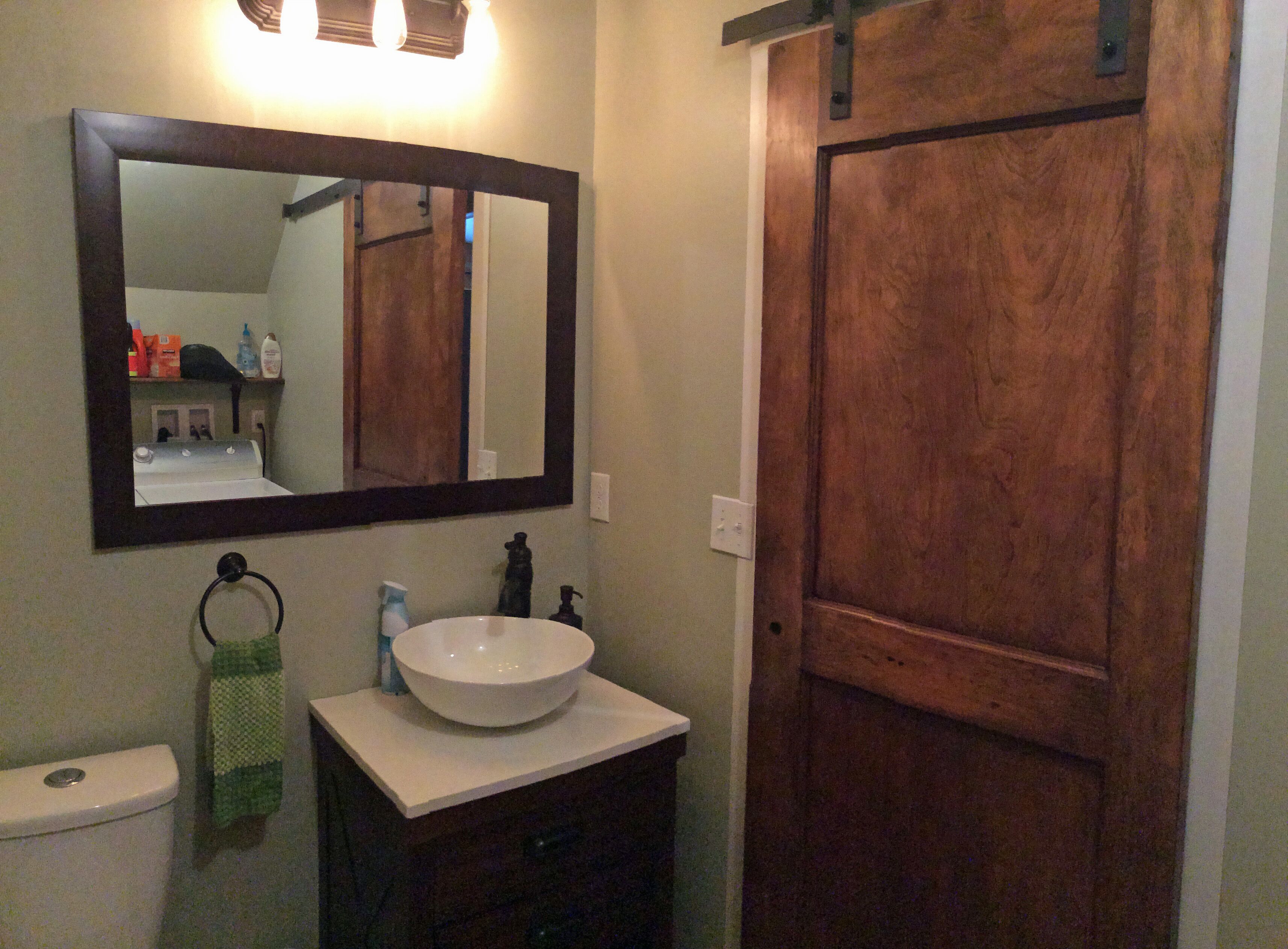 Un baño con lavamanos blanco, un espejo y una puerta de madera.