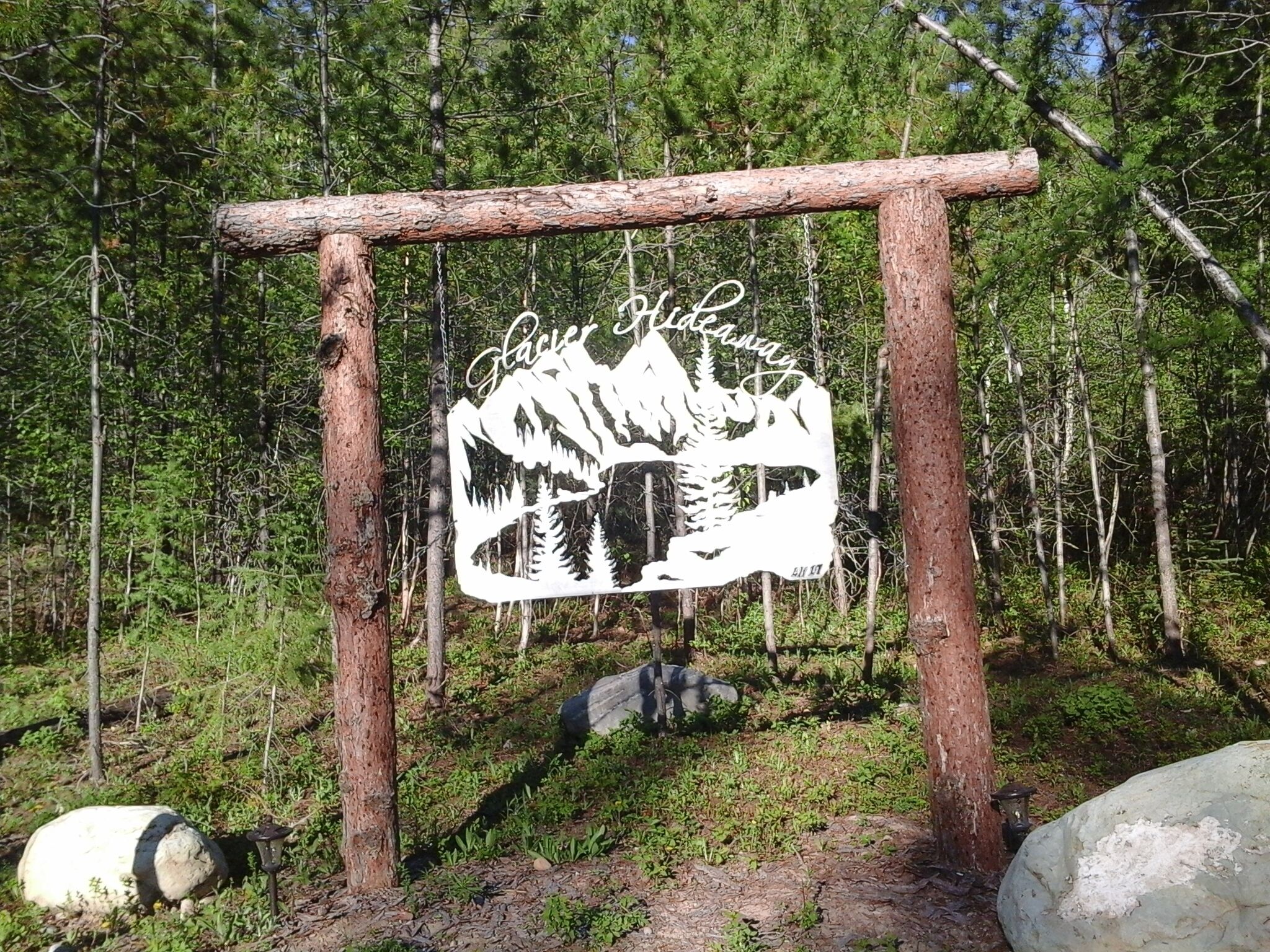 A wooden sign with a mountain and tree silhouette, reading "Glacier Lake Away."