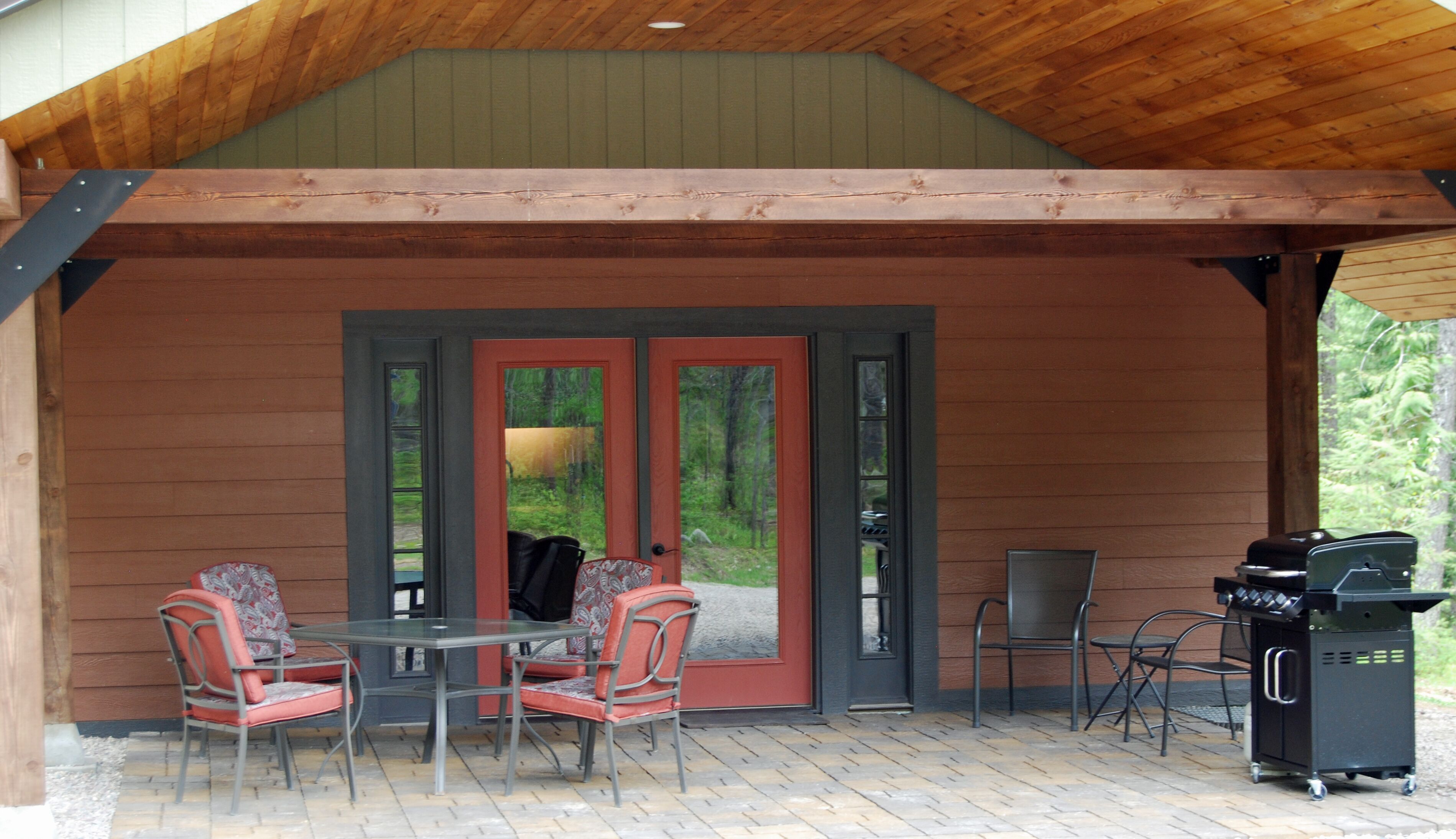 Un patio techado con una mesa, sillas, una parrilla y vistas al bosque a través de puertas de vidrio.