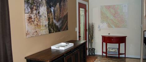 Un pasillo con una consola de madera, una puerta roja, un mapa en la pared y una pequeña mesa roja con un letrero.