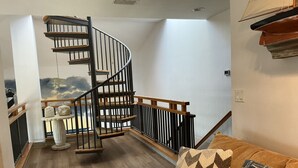 A staircase with a wooden handrail and black balusters, leading to a landing with a view of a painted landscape.