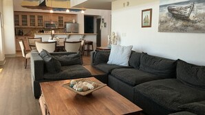 A spacious living room with dark sofas, a wooden coffee table, and a chandelier.