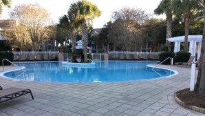 A swimming pool with a tiled deck, palm trees, and lounge chairs.