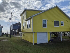 Une maison jaune à deux étages, avec une porte de garage blanche, un porche couvert et une petite terrasse.