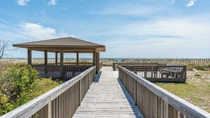 A wooden boardwalk leading to a beach pavilion with a roof, surrounded by sand dunes. - SSV 207: Oceanfront Condo with Pool and Views! (Oak Island)