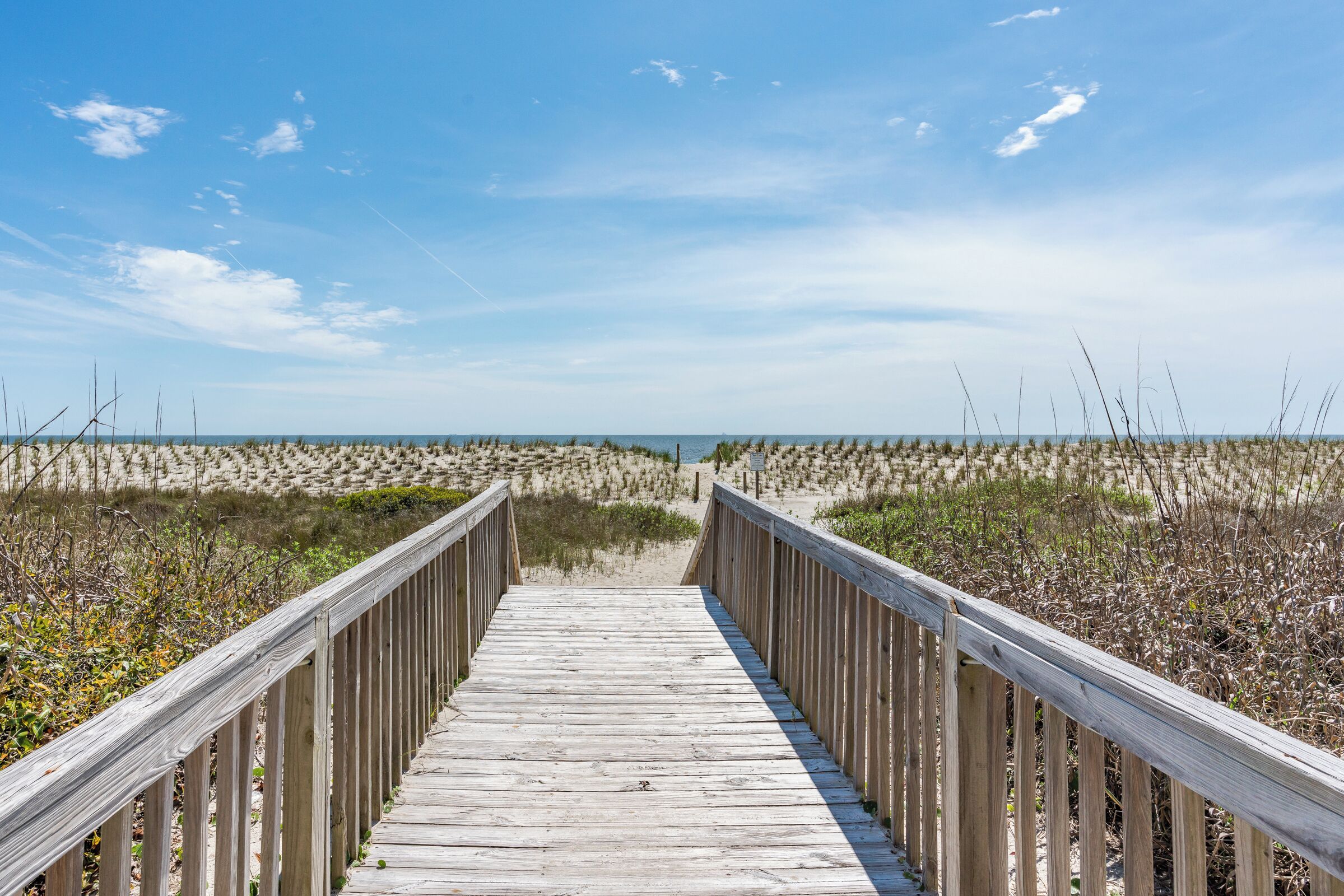 A wooden boardwalk leading to a beach with dunes and sparse vegetation.