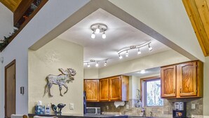A kitchen with wooden cabinets, a central island, bar stools, and a ceiling with exposed beams. - Large Beautiful Townhome, Private Hot Tub, Near Shuttle Route, In Town, WIFI (Winter Park)