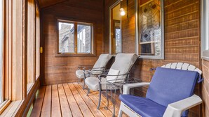 A wooden cabin with a porch, two chairs, a table, and a window with a view of buildings. - Large Beautiful Townhome, Private Hot Tub, Near Shuttle Route, In Town, WIFI (Winter Park)