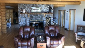 A cozy log cabin interior with a stone fireplace, leather armchairs, and a rustic wooden ceiling. - Spacious Lake Georgetown Log Home (Anaconda)