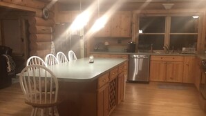 A kitchen with wooden cabinets, a stainless steel dishwasher, and a large island with chairs. - Spacious Lake Georgetown Log Home (Anaconda)