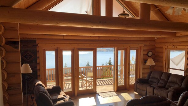 A log cabin interior with a cozy seating area, large sliding glass doors leading to a deck with a view of a lake. - Spacious Lake Georgetown Log Home (Anaconda)