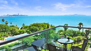 A balcony with a view of the ocean, a pool, and lush greenery.