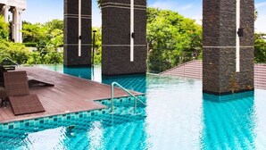 A swimming pool with a wooden deck and lounge chairs, surrounded by stone pillars and lush greenery.