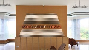 A reception area with a wooden panel wall, a sign reading "WONG AMAT TOWER," and two chairs in front.