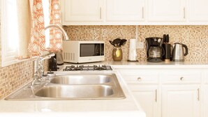 Una cocina con armarios blancos, un lavamanos doble, un microondas, una estufa a gas y una cafetera.