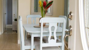 Un comedor con una mesa y sillas blancas, un espejo en la pared y una puerta con pomo dorado.