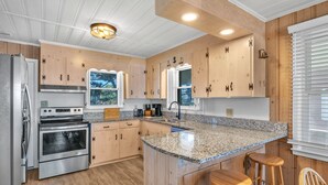 Eine moderne Küche mit Holzausstattung, Granitarbeitsplatten, Edelstahlgeräten und einer Bar mit Hockern.