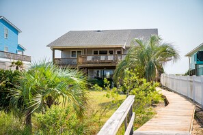 A two-story house with a balcony, surrounded by lush greenery and a wooden deck.