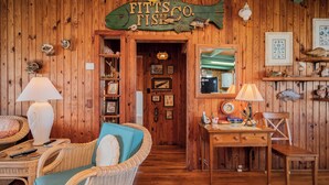 Une pièce chaleureuse, décorée d’un panneau en bois représentant un poisson, de meubles en osier, d’un bureau avec une lampe et de tableaux encadrés aux murs.