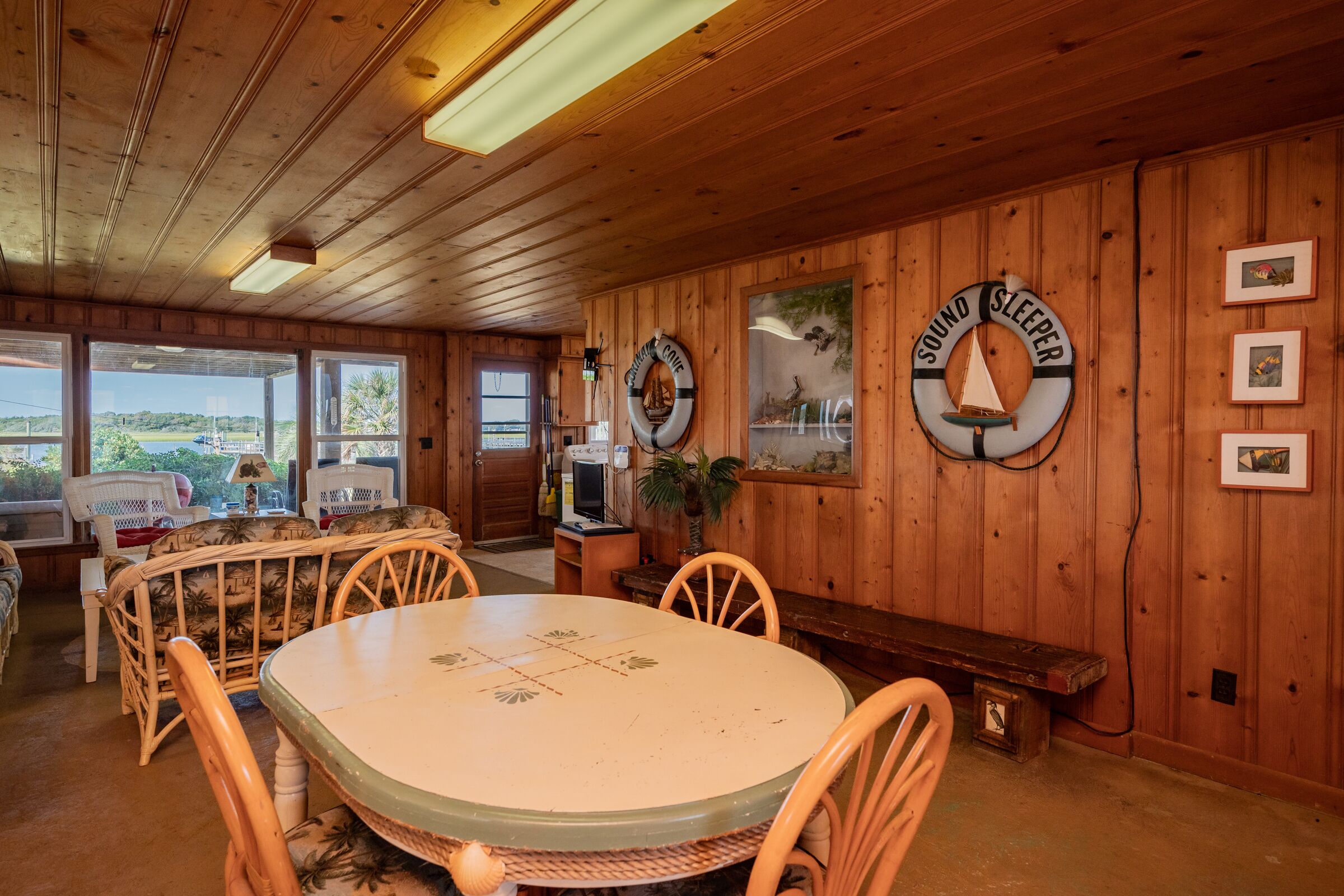 A wooden interior with a round table and chairs, a bench, and two life rings on the wall.