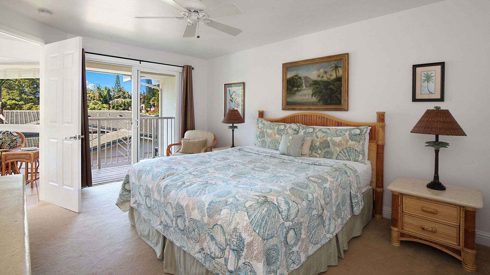 A bedroom with a large bed, a ceiling fan, a painting, and a view of the outdoors.