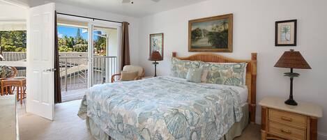 A bedroom with a large bed, a ceiling fan, a painting, and a view of the outdoors.