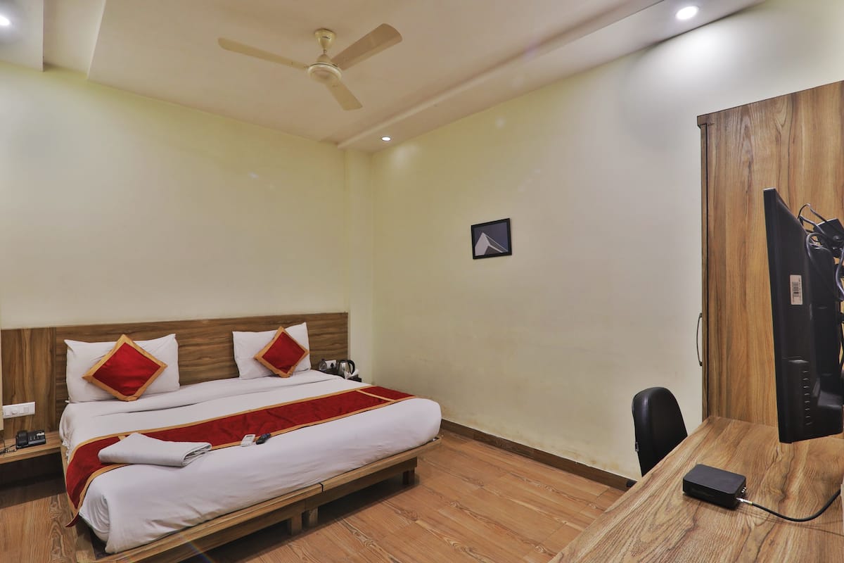 A hotel room with a bed, a desk, a chair, a TV, and a ceiling fan.