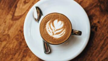 A cup of coffee with latte art on a white plate, placed on a wooden table.