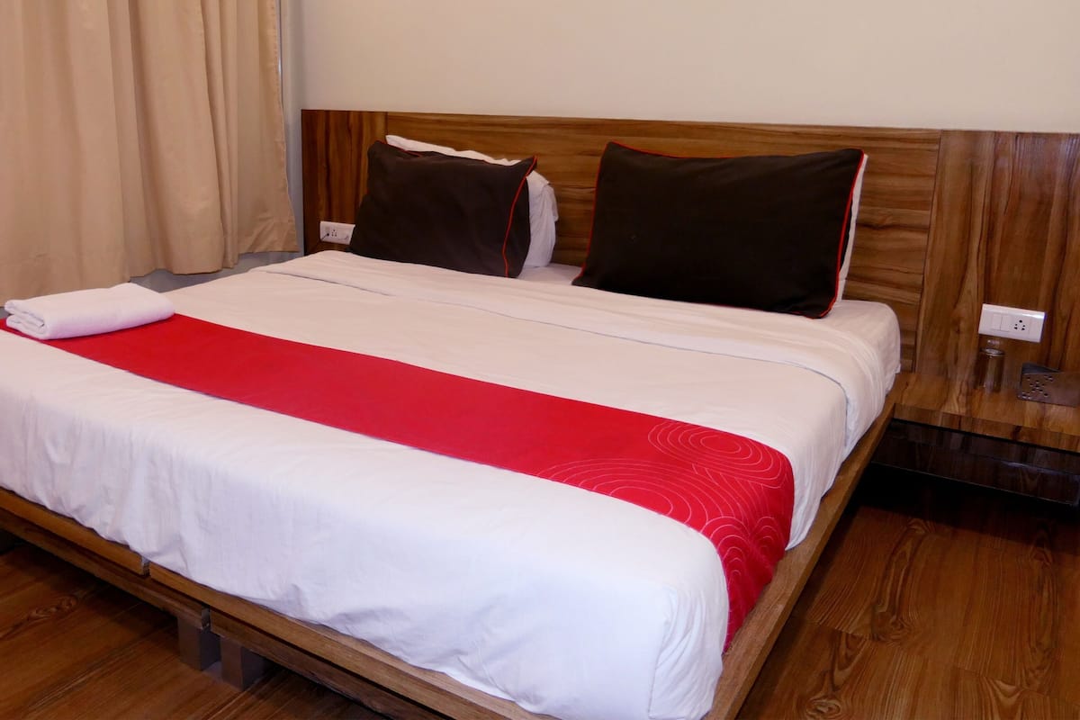 A bed with white bedding and a red accent, wooden headboard, and a wooden floor.