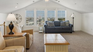 A spacious attic bedroom with a large window, a ceiling fan, and a cozy seating area with a sofa and chairs. - Sea Lookout - Great last-minute rates with ocean views. June 27-July 4! (Atlantic Beach)