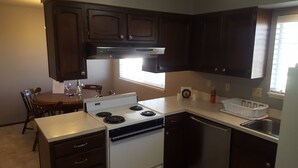 A compact kitchen with dark wooden cabinets, a white stove, and a dishwasher. - West Yakima - Clean - Safe - Netflix - 810 - ONWU-LLC (Yakima)