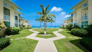 Un resort con un camino central que lleva a una palmera, rodeado de céspedes cuidados y vistas al océano.