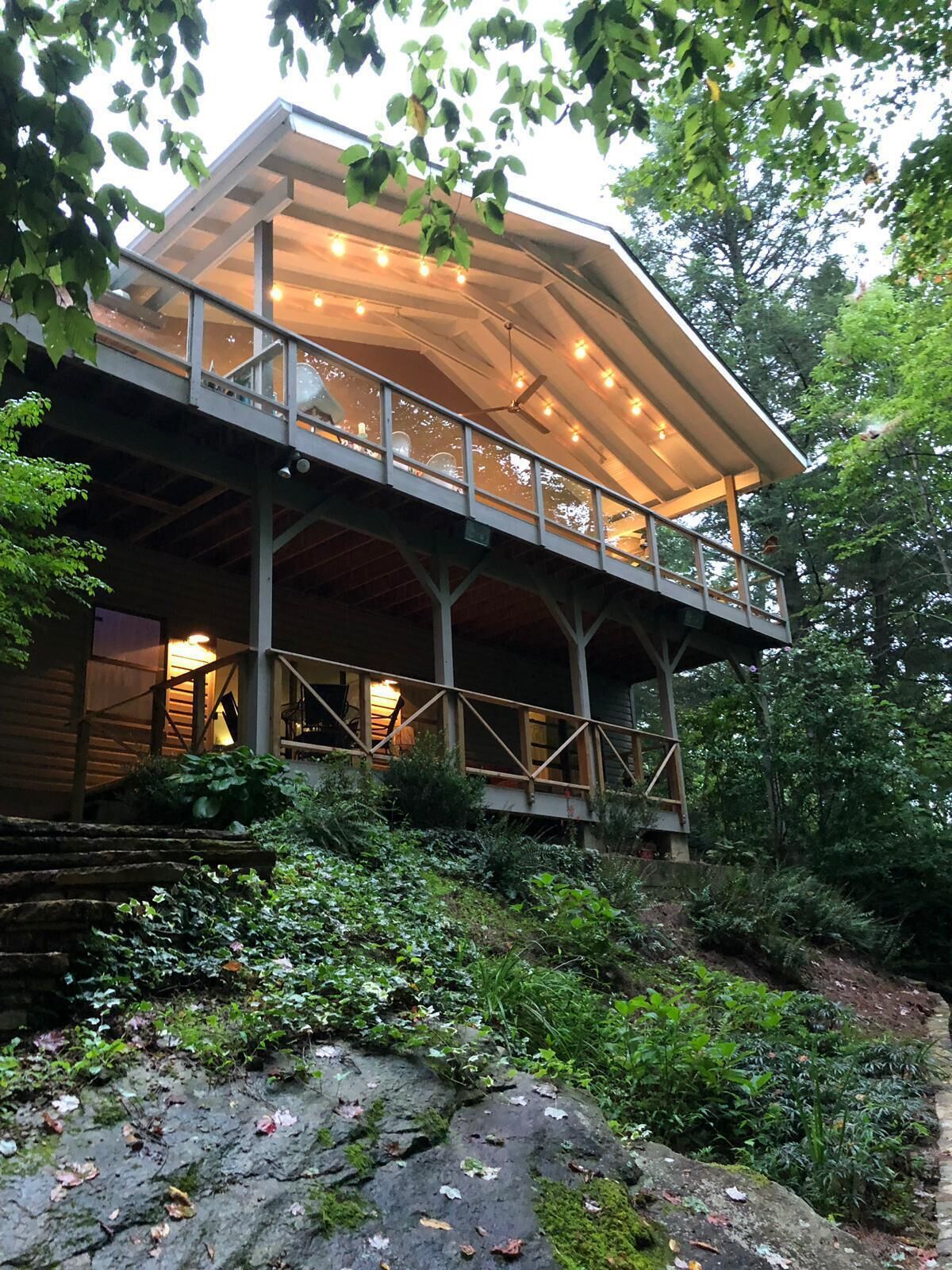 A modern building with a glass balcony, surrounded by lush greenery and a stone pathway.
