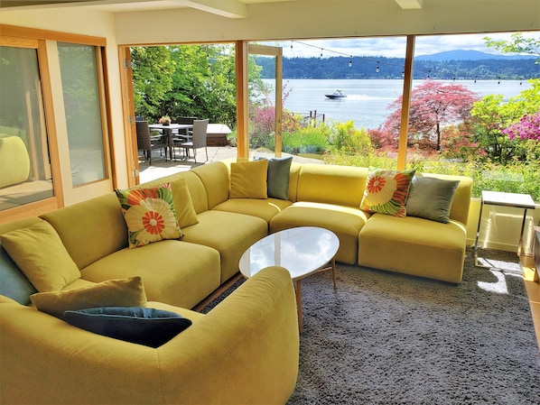 Una sala de estar moderna con un sofá seccional amarillo, una mesa de centro redonda y vista a un lago con barcos.