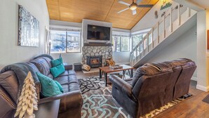 A living room with a stone fireplace, leather sofa, and a staircase. - Fully Remodeled Condo Near Gondola & Village 276 (Mammoth Lakes)