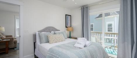Un dormitorio con cama, mesita de noche, una silla, ventana y balcón.