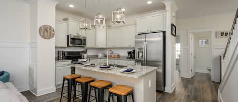 A modern kitchen with white cabinets, stainless steel appliances, and a central island with bar stools.