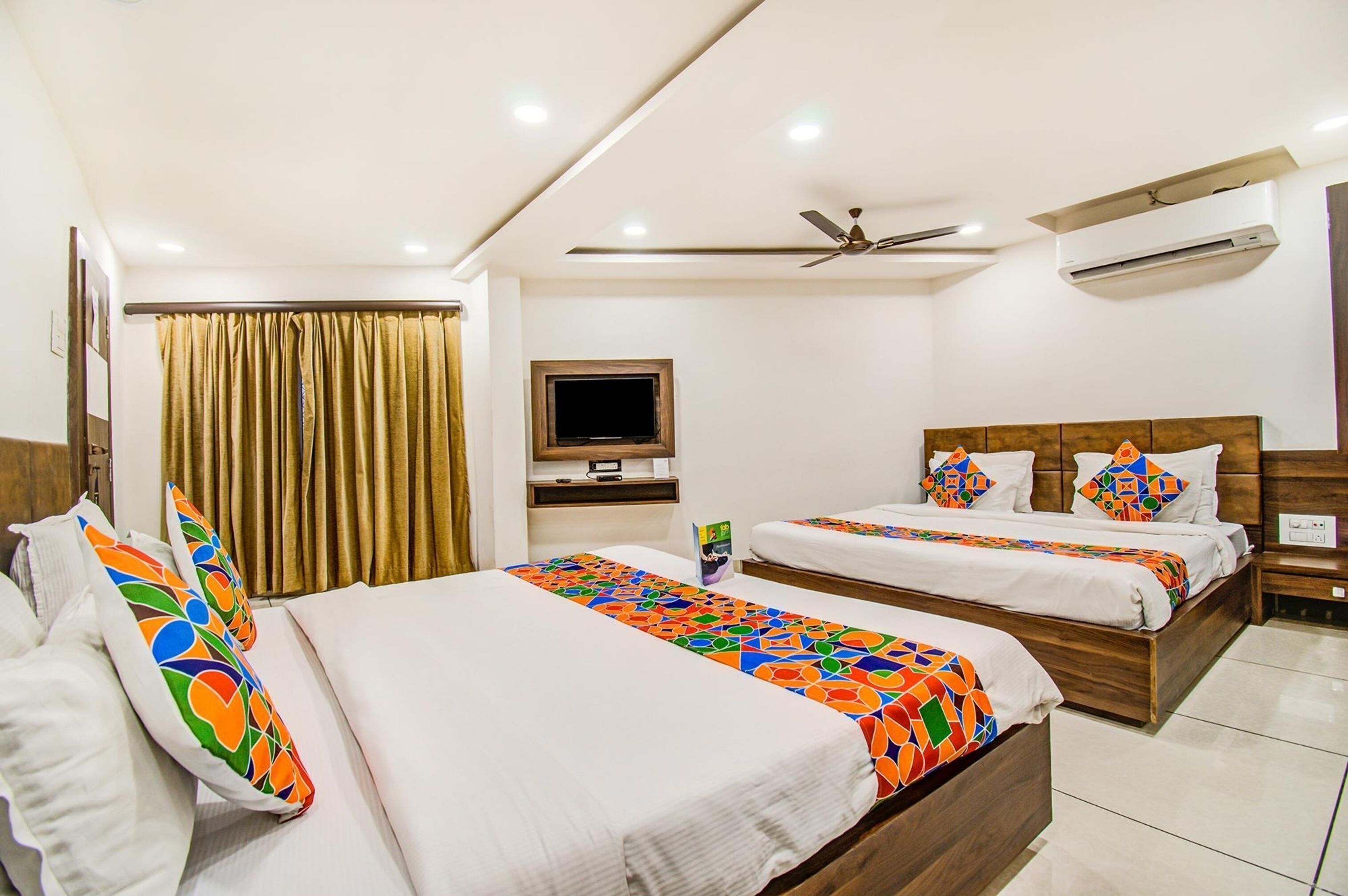 A hotel room with two beds, a TV, a ceiling fan, and an air conditioning unit.
