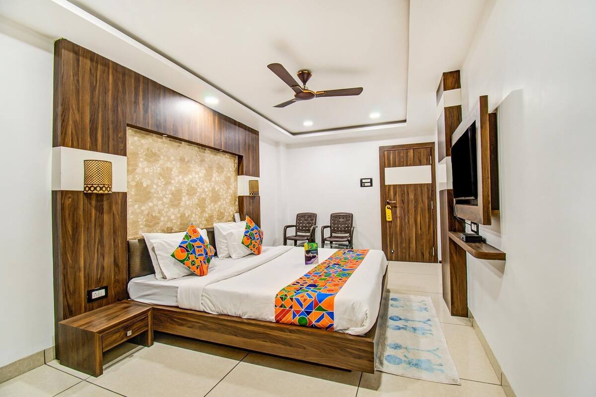 A bedroom with a wooden bed, a ceiling fan, a TV, and a small seating area with chairs.