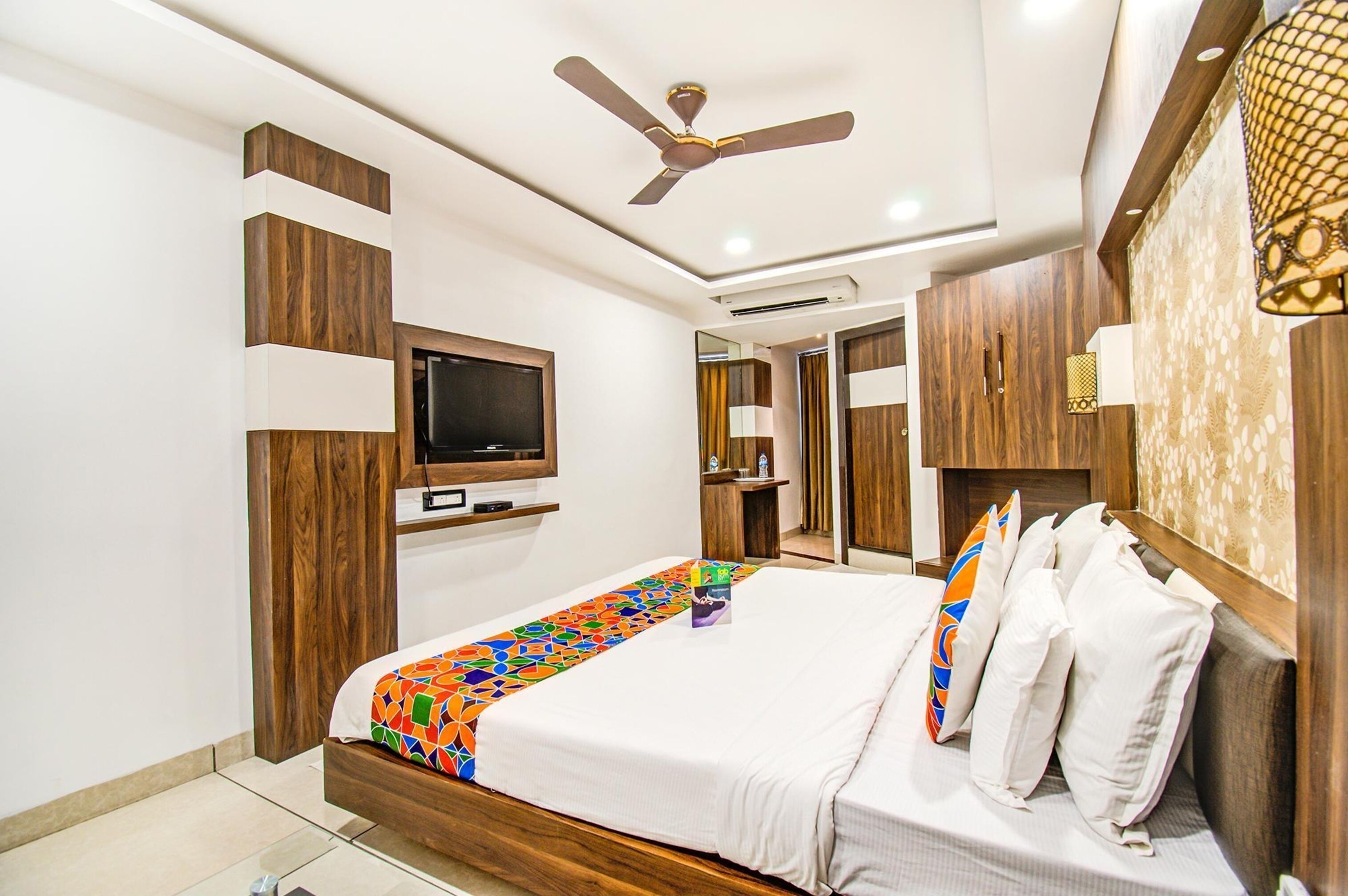 A modern bedroom with a bed, a ceiling fan, a TV, and wooden paneling.