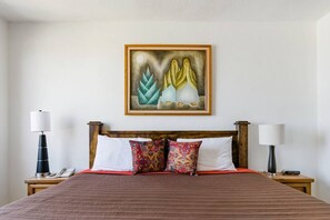 A hotel room with a large bed, two bedside tables, a nightstand, a wall-mounted painting, and a wooden headboard. - Cozy Mexican Style Cottage  Walking Distance to Beach  Affordable Cabo Retreat for Long and Short Stays (Cabo San Lucas)