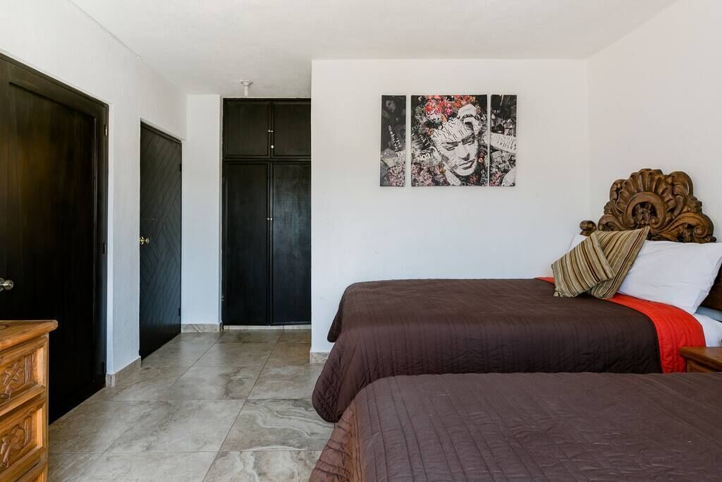 Ein Schlafzimmer mit zwei Betten, einer hölzernen Kommode, einem dunklen Kleiderschrank und einer Wand mit zwei gerahmten Kunstwerken.